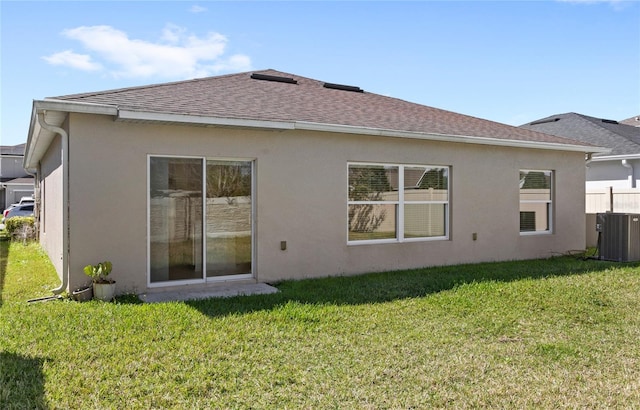 rear view of property with a yard, roof with shingles, central AC, and stucco siding