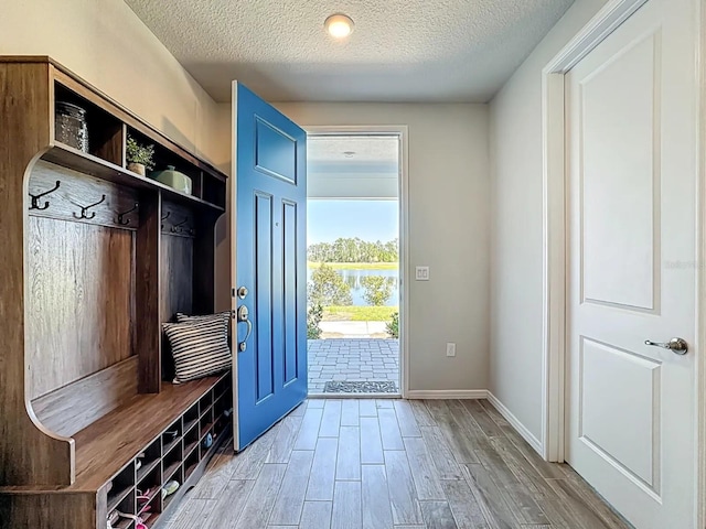 mudroom featuring a textured ceiling, baseboards, wood finish floors, and a water view