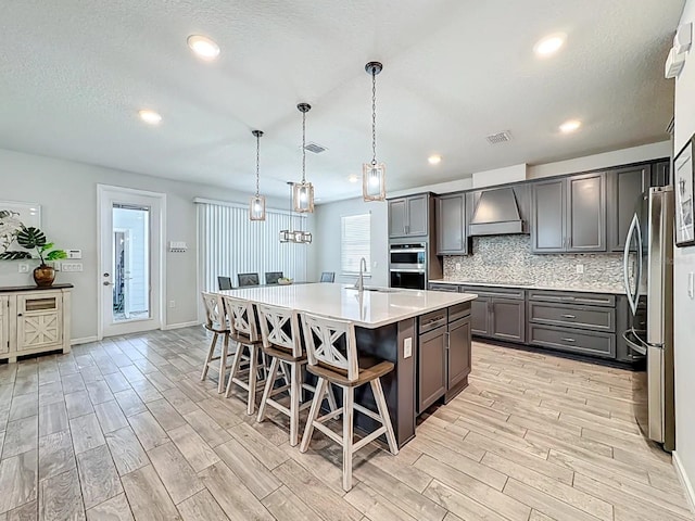 kitchen with wood tiled floor, premium range hood, backsplash, and stainless steel appliances