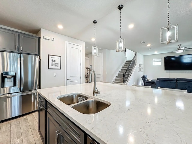 kitchen with light wood finished floors, a sink, stainless steel refrigerator with ice dispenser, pendant lighting, and open floor plan