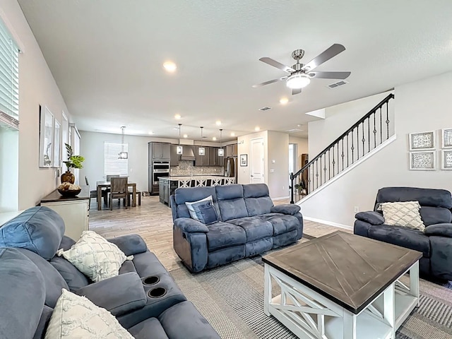 living room featuring stairway, visible vents, baseboards, recessed lighting, and light wood-style floors