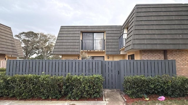 view of home's exterior with mansard roof, fence, and brick siding