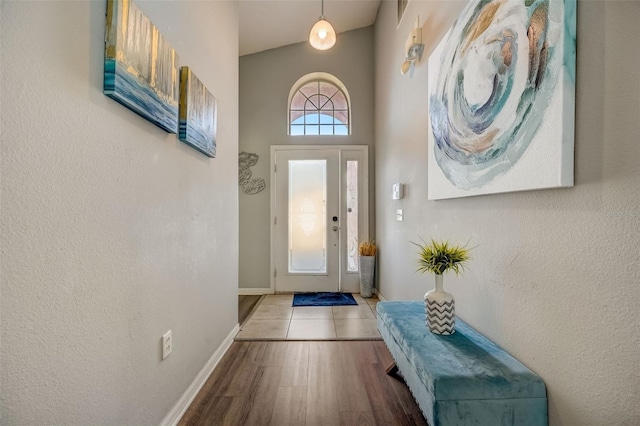 doorway to outside featuring wood finished floors, baseboards, and a towering ceiling