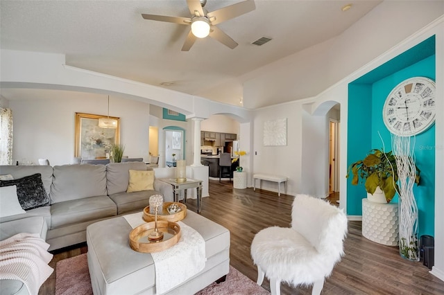 living room with wood finished floors, visible vents, decorative columns, arched walkways, and vaulted ceiling