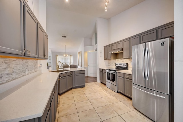 kitchen featuring a peninsula, light tile patterned flooring, a sink, appliances with stainless steel finishes, and tasteful backsplash