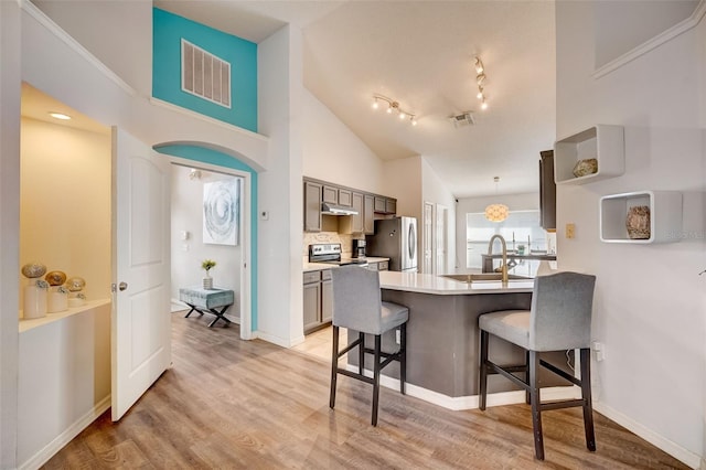 kitchen with a kitchen bar, visible vents, under cabinet range hood, appliances with stainless steel finishes, and a peninsula