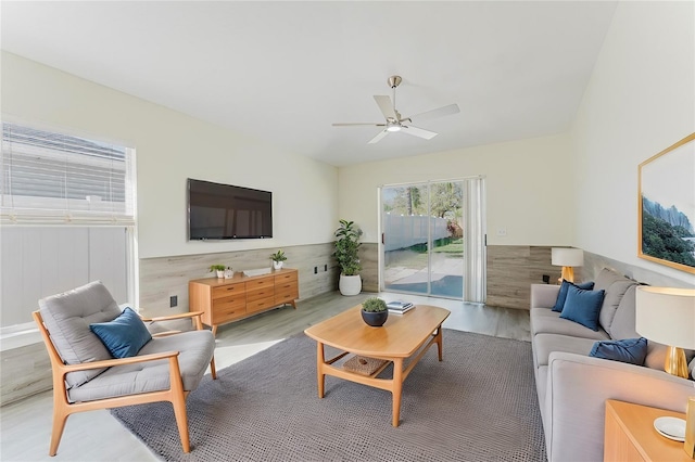 living room featuring ceiling fan, wooden walls, wood finished floors, and wainscoting