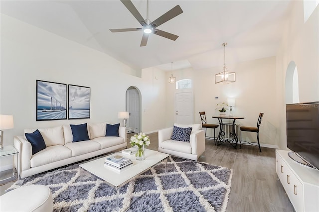 living room featuring ceiling fan, baseboards, vaulted ceiling, light wood-style floors, and arched walkways