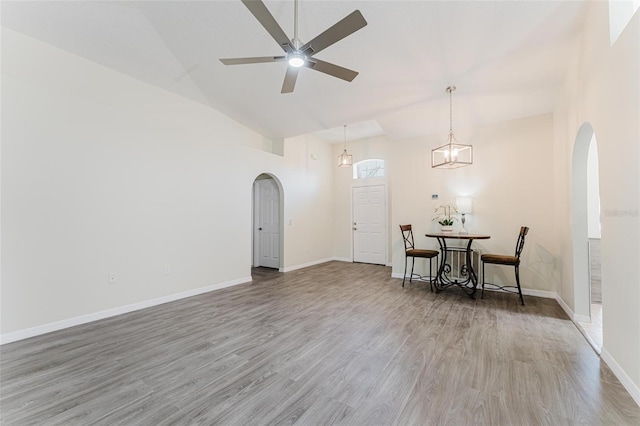 interior space featuring a ceiling fan, wood finished floors, baseboards, arched walkways, and vaulted ceiling