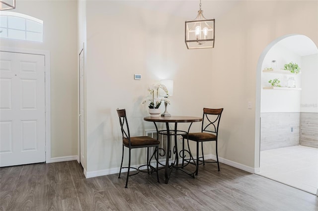 dining space featuring baseboards, arched walkways, wood finished floors, and a chandelier