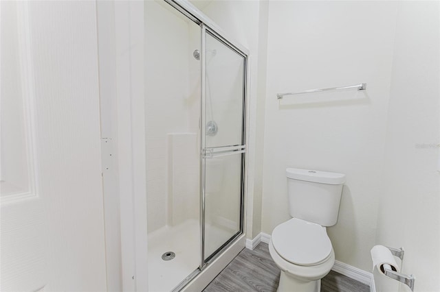 bathroom featuring toilet, wood finished floors, a stall shower, and baseboards