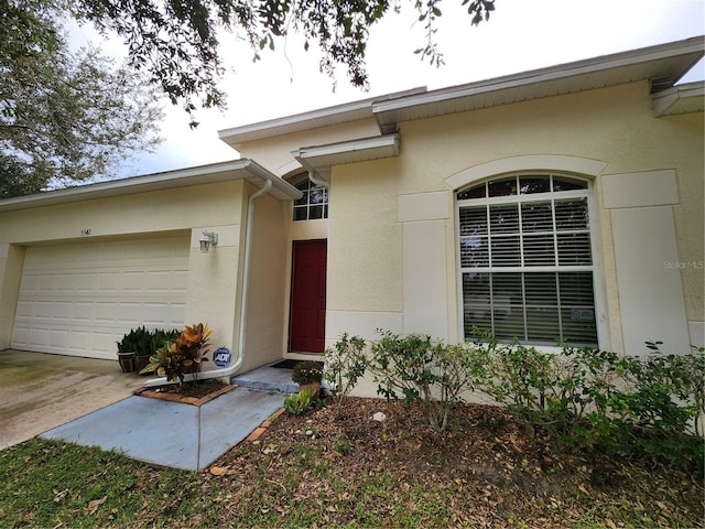 entrance to property with stucco siding, concrete driveway, and a garage