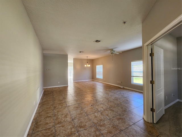 tiled spare room with a textured ceiling, ceiling fan with notable chandelier, visible vents, and baseboards