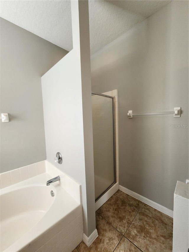 bathroom featuring baseboards, a stall shower, a textured ceiling, tile patterned floors, and a bath