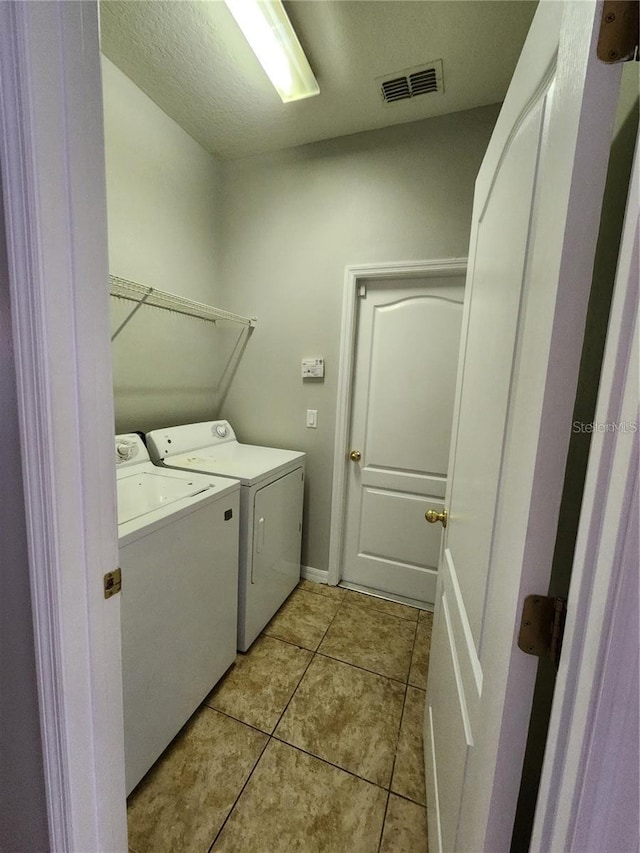 washroom featuring visible vents, washer and clothes dryer, laundry area, light tile patterned flooring, and a textured ceiling