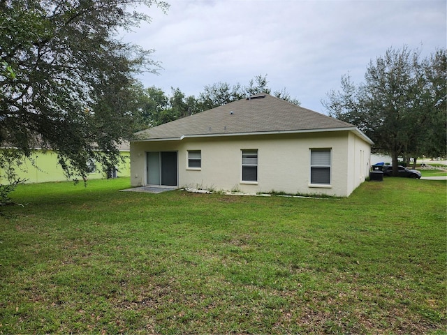 rear view of house with a lawn, roof with shingles, and stucco siding