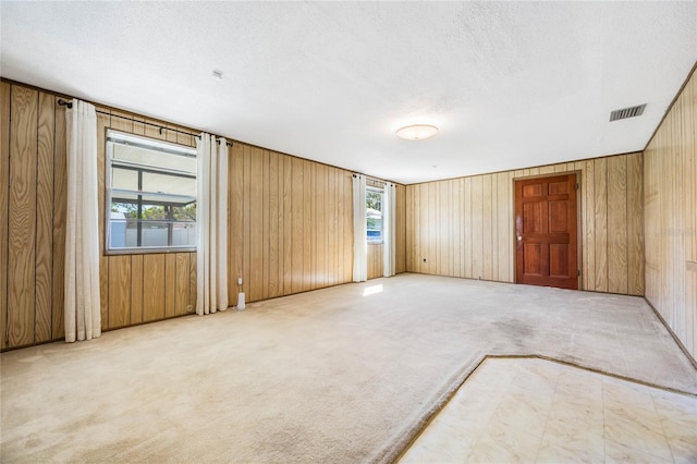 spare room featuring visible vents, a textured ceiling, wooden walls, and carpet floors