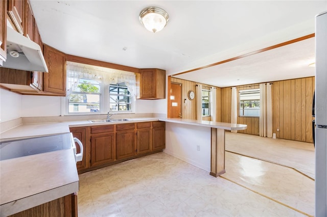 kitchen with wood walls, light countertops, a peninsula, brown cabinetry, and a sink