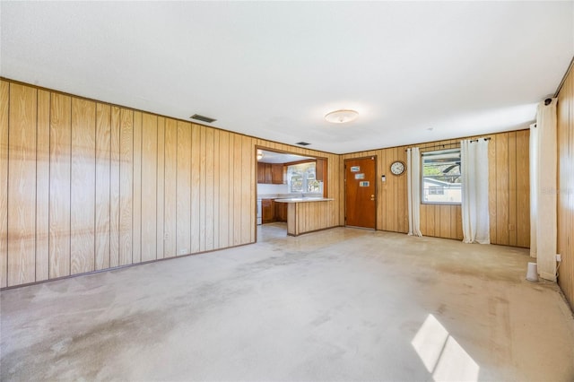 unfurnished living room with visible vents, wooden walls, and light colored carpet