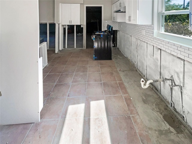 kitchen with under cabinet range hood, stove, white cabinets, and light tile patterned floors