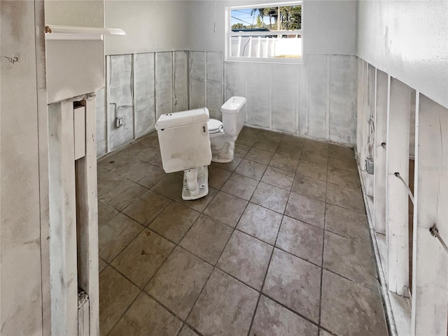 bathroom with a wainscoted wall, toilet, and tile patterned flooring