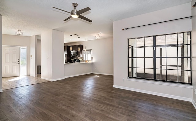 unfurnished living room featuring dark wood-style floors, baseboards, a textured ceiling, and a ceiling fan