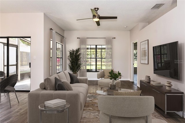 living area with visible vents, a textured ceiling, wood finished floors, baseboards, and ceiling fan