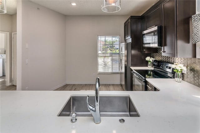 kitchen with light wood-style flooring, a sink, decorative backsplash, light countertops, and appliances with stainless steel finishes