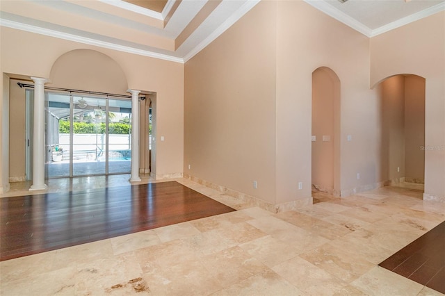 empty room featuring arched walkways, a high ceiling, ornamental molding, and ornate columns