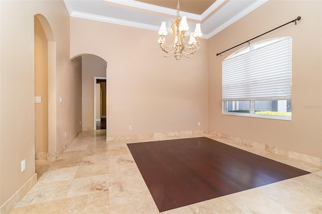 spare room with a tray ceiling, arched walkways, crown molding, baseboards, and a chandelier