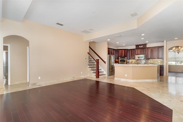 unfurnished living room with arched walkways, visible vents, light wood-style flooring, and stairway