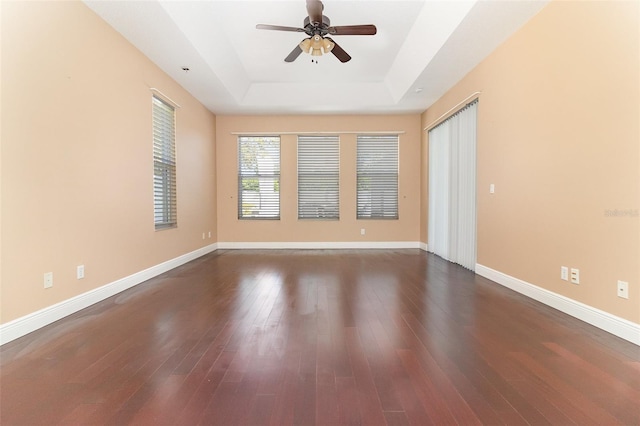 empty room with dark wood finished floors, a raised ceiling, a ceiling fan, and baseboards