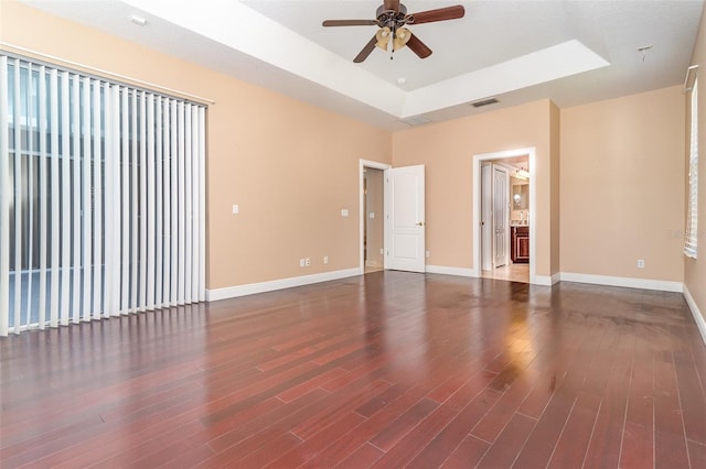 spare room with visible vents, a tray ceiling, wood finished floors, baseboards, and ceiling fan