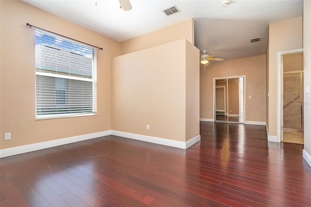 empty room with dark wood finished floors, a ceiling fan, visible vents, and baseboards