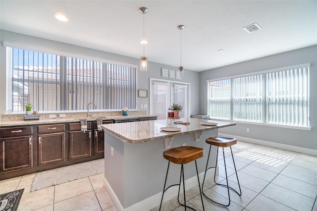 kitchen with a kitchen breakfast bar, a center island, light tile patterned floors, light stone countertops, and dark brown cabinets