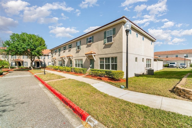 view of front facade with a residential view, stucco siding, central AC, and a front yard