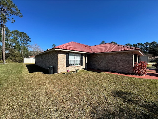 view of side of property with a lawn, brick siding, and metal roof