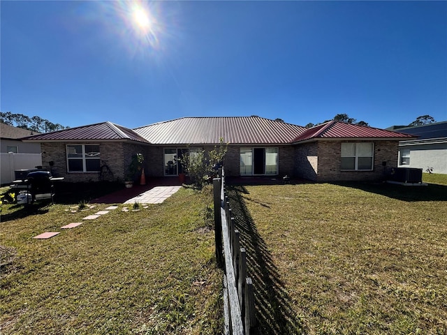 view of front facade featuring brick siding, a front lawn, fence, central air condition unit, and metal roof