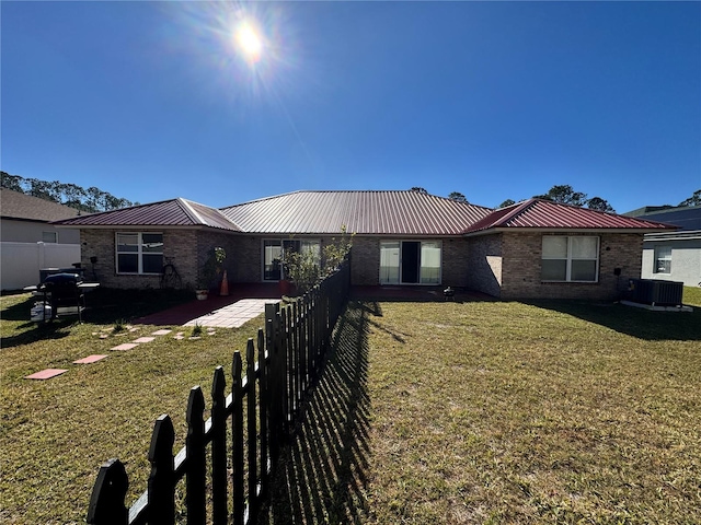 ranch-style home featuring brick siding, a front lawn, fence, metal roof, and a patio area