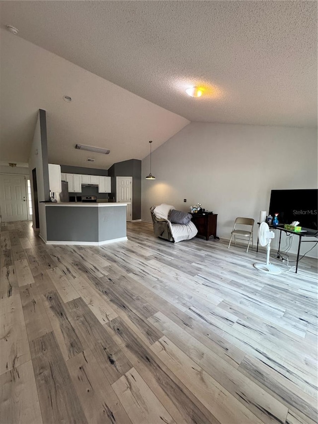 unfurnished living room with vaulted ceiling, light wood-style flooring, and a textured ceiling