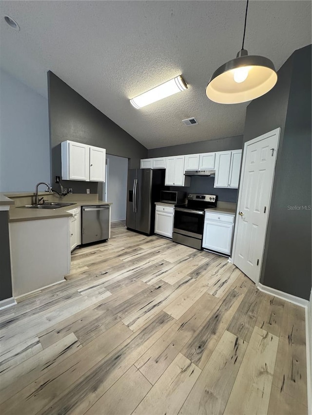 kitchen featuring under cabinet range hood, lofted ceiling, appliances with stainless steel finishes, white cabinetry, and a sink