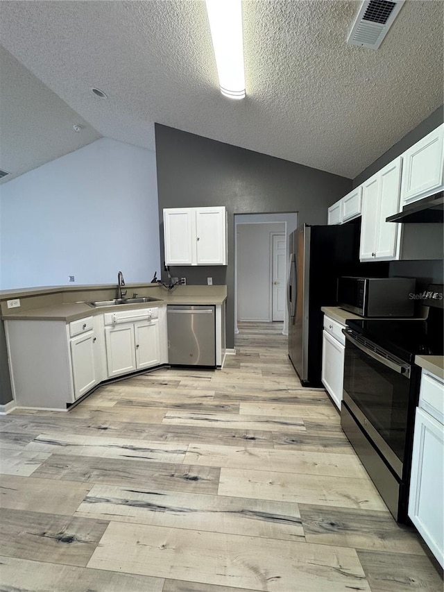 kitchen featuring lofted ceiling, a peninsula, a sink, white cabinets, and appliances with stainless steel finishes