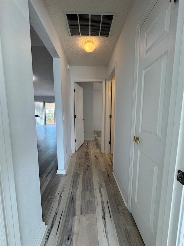 corridor featuring visible vents, a textured ceiling, light wood-type flooring, and baseboards