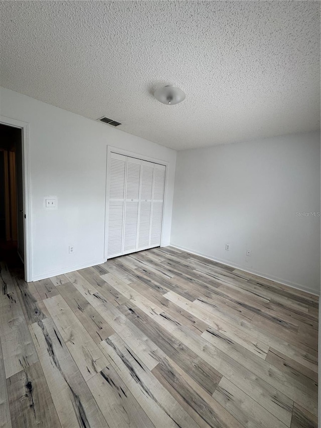 unfurnished bedroom featuring a closet, visible vents, a textured ceiling, and wood finished floors