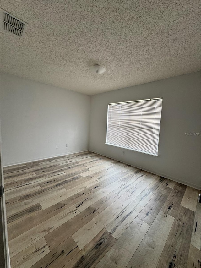 unfurnished room with visible vents, a textured ceiling, and hardwood / wood-style floors