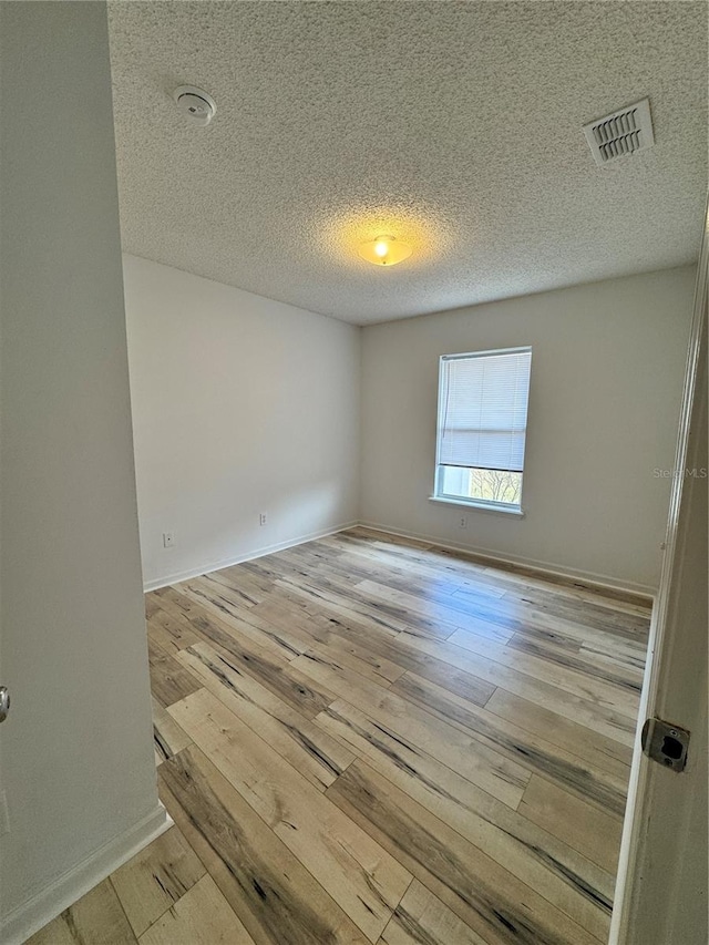 unfurnished room with visible vents, a textured ceiling, light wood-type flooring, and baseboards