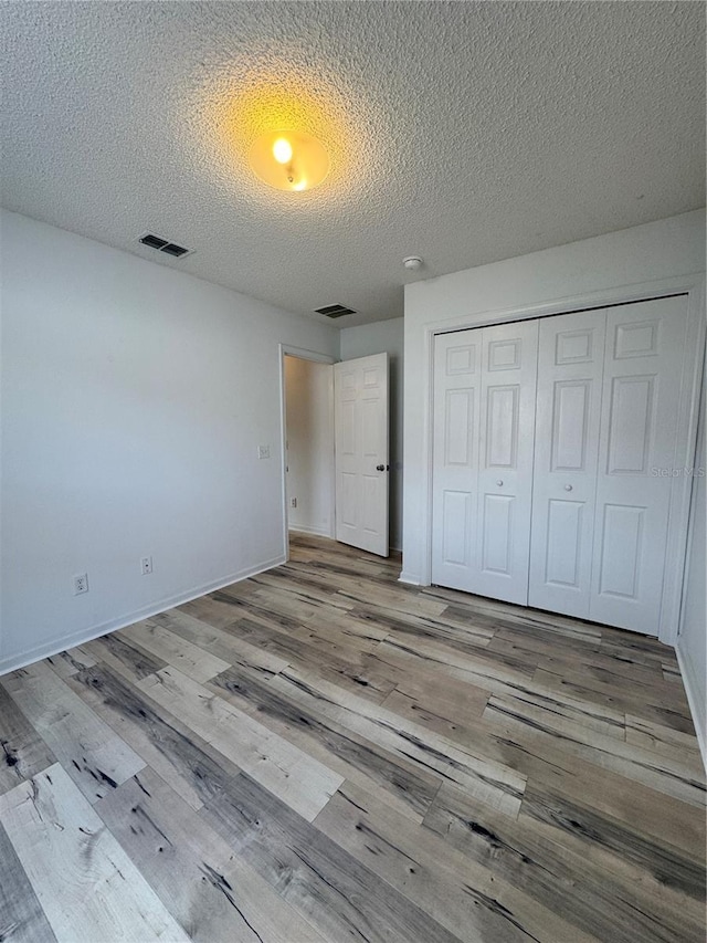 unfurnished bedroom with visible vents, a closet, and wood finished floors