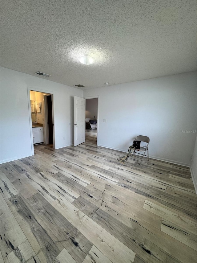 empty room with visible vents, light wood-style flooring, and a textured ceiling