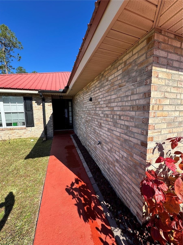 doorway to property with metal roof, brick siding, and a yard