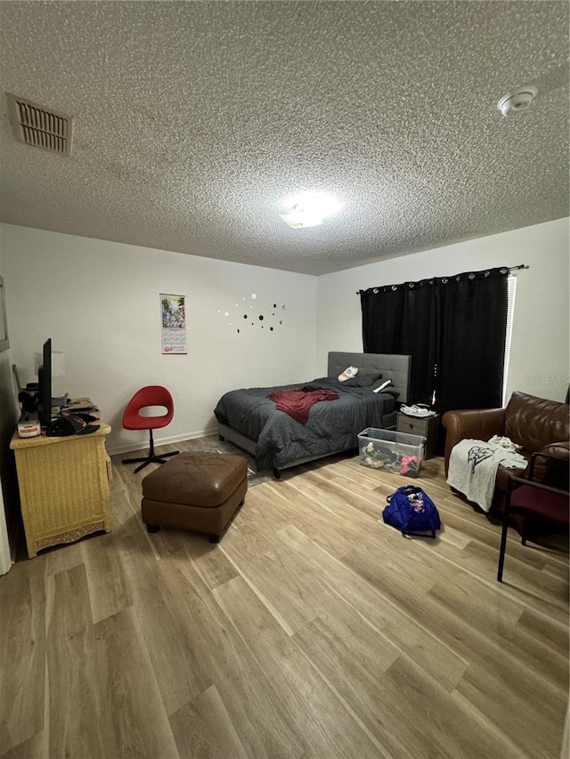 bedroom with visible vents, a textured ceiling, and wood finished floors